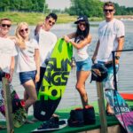 atrakcje Mielno - grupa młodych przyjaciół stroi na pomoście i trzyma deskę do pływania